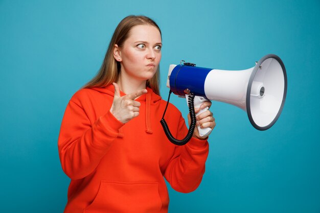 Impressed young blonde woman holding speaker looking and pointing at side with pursed lips 