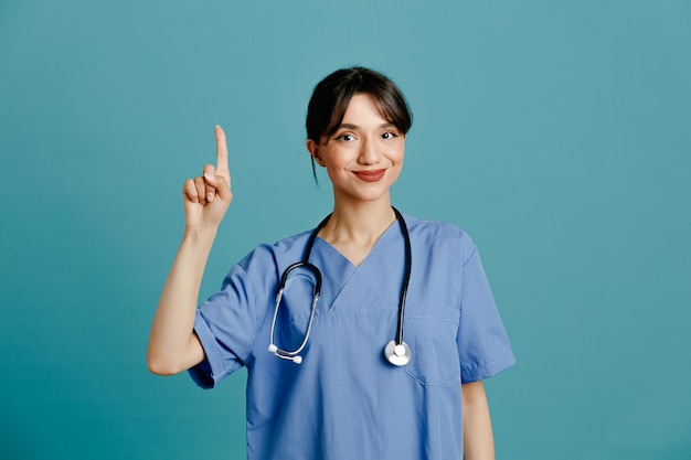 Впечатленная молодая женщина-врач в униформе, изолированная на синем фоне