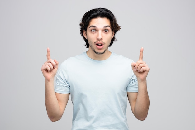 impressed young handsome man looking at camera pointing fingers up isolated on white background