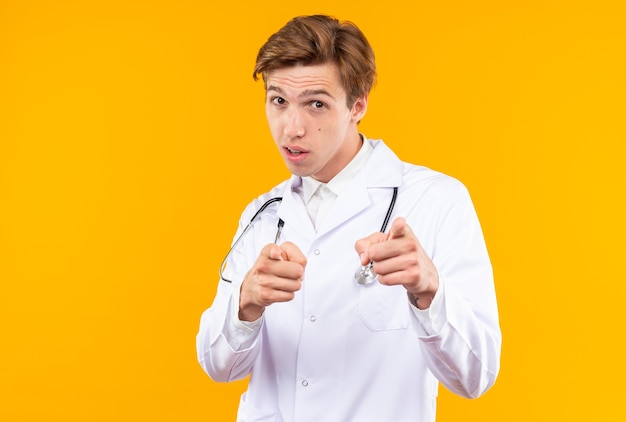 Impressed young male doctor wearing medical robe with stethoscope points at front