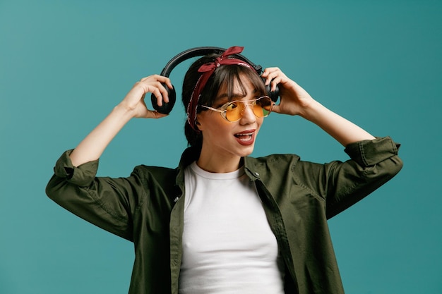 Photo impressed young student girl wearing bandana sunglasses holding headphones around head looking at side isolated on blue background