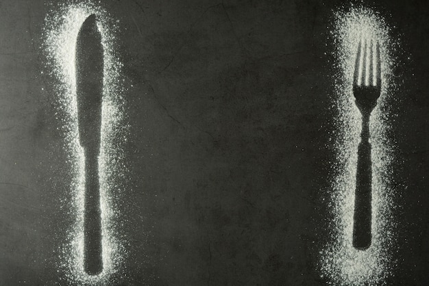 Imprint fork and knife silhouette made of flour on a black background 