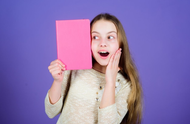 Improving herself through education Surprised little girl with open mouth holding education book with rosy cover Cute small child getting formal education in primary school Education copy space