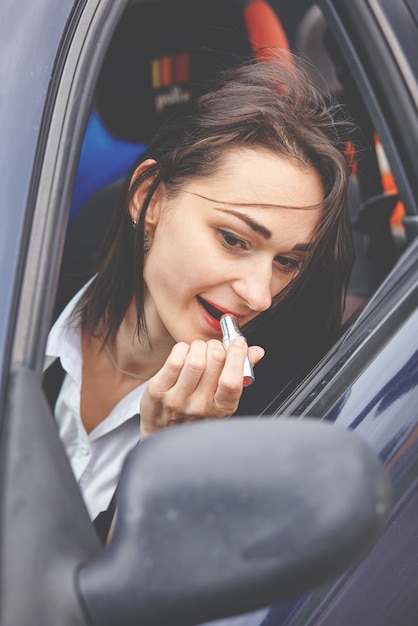 軽率な運転/運転中に口紅を塗る若い女性