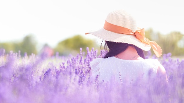 写真 紫のラベンダー畑では、花の間で麦わら帽子をかぶった女性が後ろからしか見えません