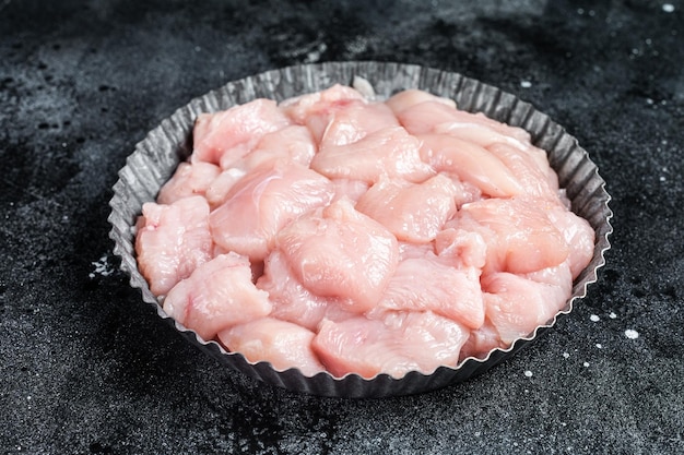 In blokjes gesneden rauwe kippenborstfilets op een bord pluimveevlees Zwarte achtergrond Bovenaanzicht