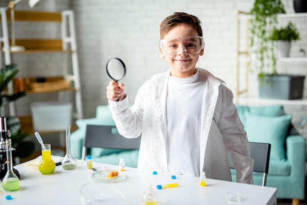 Фото В классе химии маленький улыбающийся мальчик держит увеличительное стекло