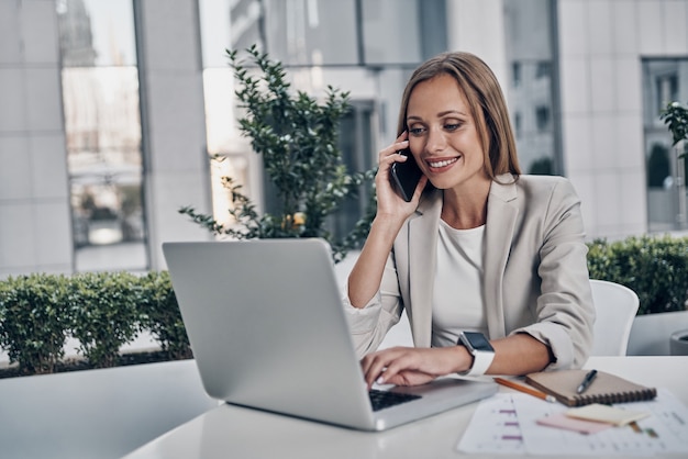 In contact met opdrachtgevers. Mooie jonge vrouw die aan de telefoon praat en glimlacht