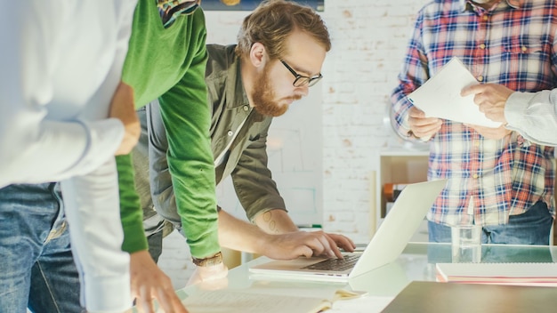 Foto in creatief kantoor productieve collega's staan aan de tafel met strategische planningssessie ze werken op laptops uitwisselen notities brengen mappen met grafieken