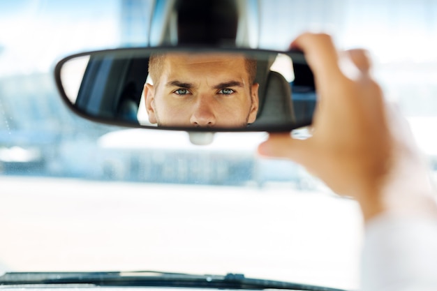 Foto in de auto. sluit omhoog van een achteruitkijkspiegel met een slimme bekwame bestuurder die ernaar kijkt