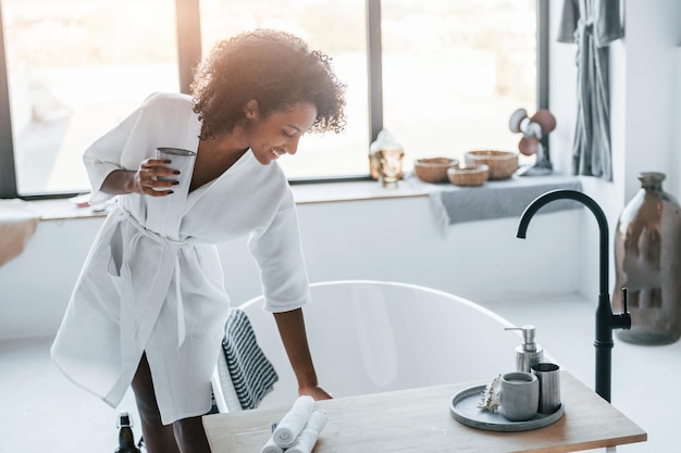 In de badkamer Jonge Afro-Amerikaanse vrouw met krullend haar binnenshuis thuis