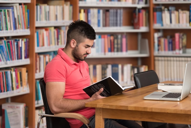 In de bibliotheek Knappe Arabische mannelijke student met laptop en boeken werken in een middelbare school Universiteitsbibliotheek ondiepe scherptediepte