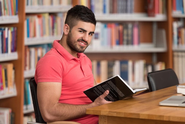 In de bibliotheek Knappe Arabische mannelijke student met laptop en boeken werken in een middelbare school Universiteitsbibliotheek ondiepe scherptediepte