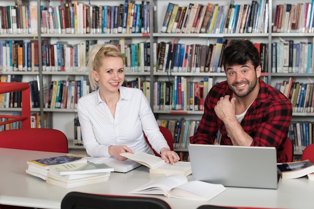 In de bibliotheek knappe twee studenten met laptop en boeken werken in een middelbare school Universiteitsbibliotheek
