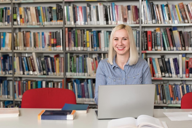 In de bibliotheek Mooie vrouwelijke student met boeken die in een middelbare school werken Universiteitsbibliotheek Ondiepe scherptediepte