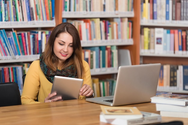 In de bibliotheek mooie vrouwelijke student met laptop en boeken werken in een middelbare school Universiteitsbibliotheek ondiepe scherptediepte