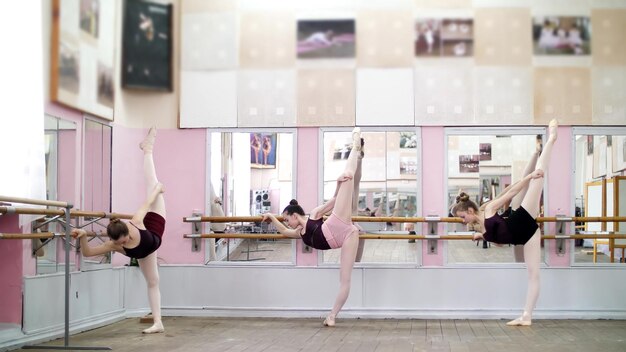 Foto in de danszaal strekken jonge ballerinas in zwarte leotards zich uit bij de barre.