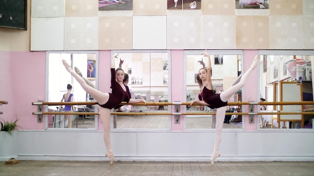 Foto in de danszaal voeren jonge ballerinas in paarse leotards een grand battement uit op pointe schoenen.