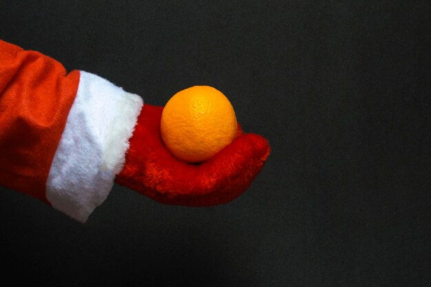 In de hand van de kerstman een mandarijn op een zwarte achtergrond. Nieuwjaarsconcept