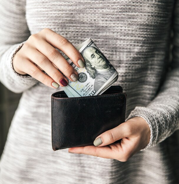 In de handen van de vrouwen ligt de bruinleren portemonnee met een prop van honderd dollar.