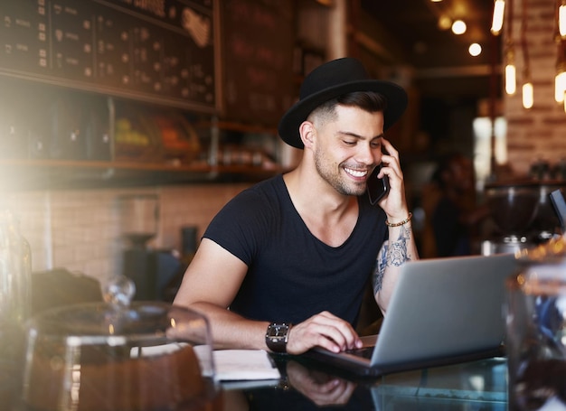 In de koffie-industrie kun je het beste draadloos gaan Shot van een jonge man die een telefoon en laptop gebruikt terwijl hij in een coffeeshop werkt