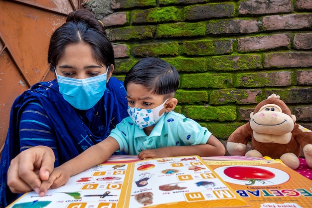 In de lockdown en thuisquarantaine van de Covid19-epidemie geeft een Aziatische moeder haar kind thuis les met een masker op in Joypara Dohar Dhaka, Bangladesh
