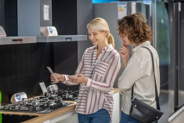 In de megastore. Verkoopassistent in gestreept overhemd in gesprek met vrouwelijke klant