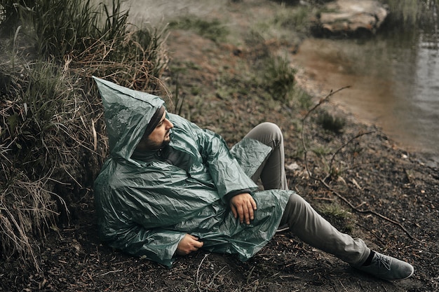 In de natuur zit een man in een groene regenjas op de grond