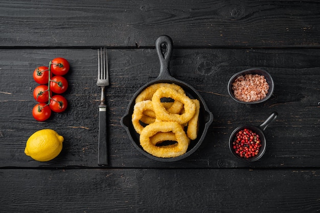 In de oven gebakken gepaneerde calamaresringen op gietijzeren koekenpan, op zwarte houten tafelachtergrond, bovenaanzicht plat gelegd, met kopieerruimte voor tekst