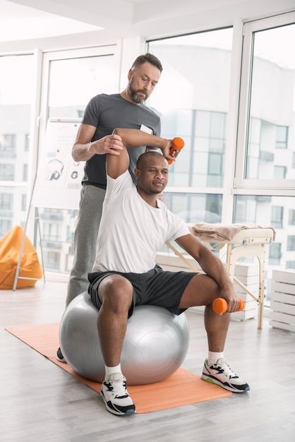 In de sportschool. Aardige jongeman met behulp van sportartikelen tijdens het trainen met een persoonlijke coach