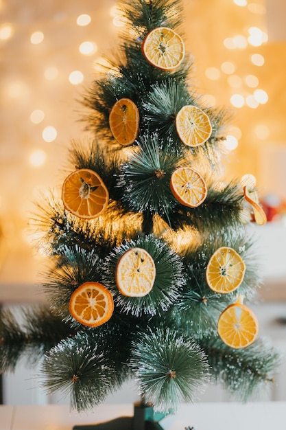 In de winter is de boom buiten versierd met gedroogde sinaasappels, groene takken tegen een wazige achtergrond en geelgouden bokeh. Feestelijke inrichting in eco-stijl. Vrolijk kerstfeest.