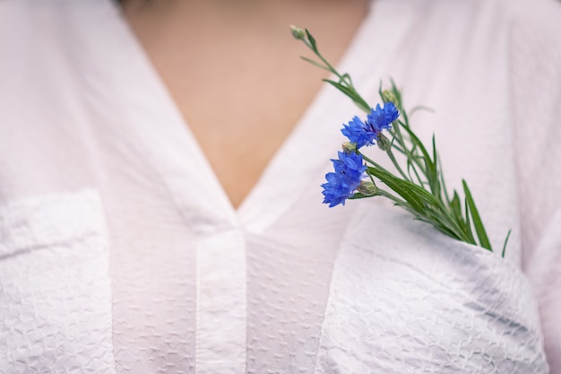 In de zak van de witte blouse van het meisje zitten twee blauwe korenbloemen.