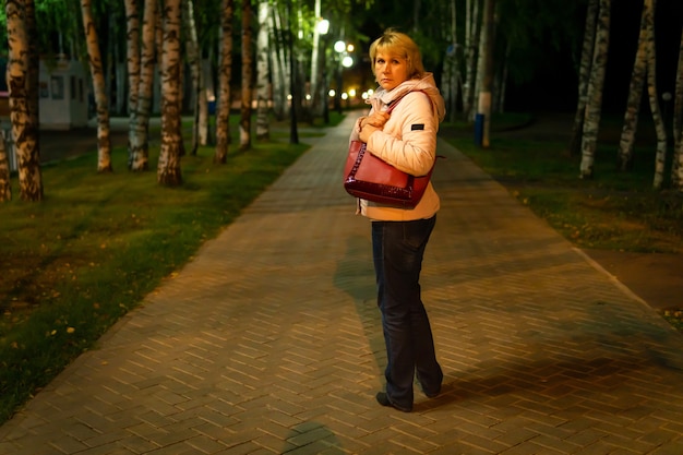 In een donkere nacht park op het pad is een vrouw, ze is bang, straatverlichting shine, het is donker rond.