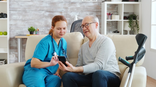 In een helder en gezellig bejaardentehuis helpt maatschappelijk werker een oude man om een smartphone te gebruiken.