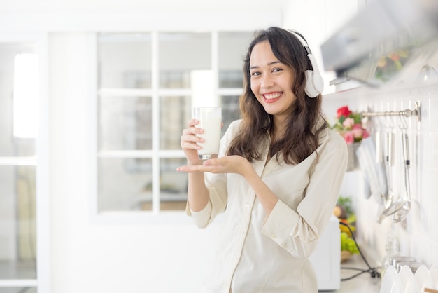 In een lichte moderne keuken drinkt een mooie vrouw melk terwijl ze naar muziek luistert. Voor het ontbijt vermaakt ze zich en lacht ze.