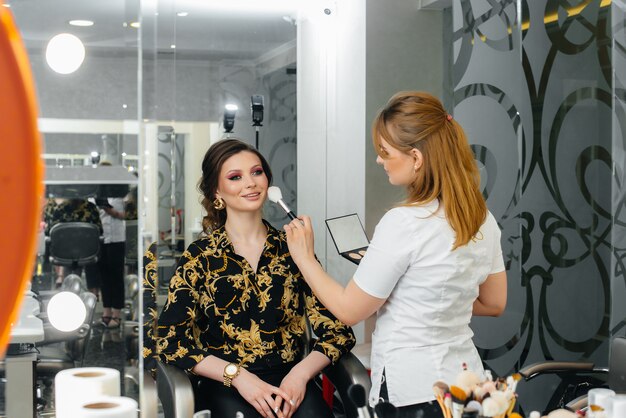 In een mooie, moderne schoonheidssalon maakt een professionele make-upstylist make-up voor een jong meisje. Schoonheid en mode.