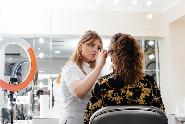 In een mooie, moderne schoonheidssalon maakt een professionele make-upstylist make-up voor een jong meisje. Schoonheid en mode.