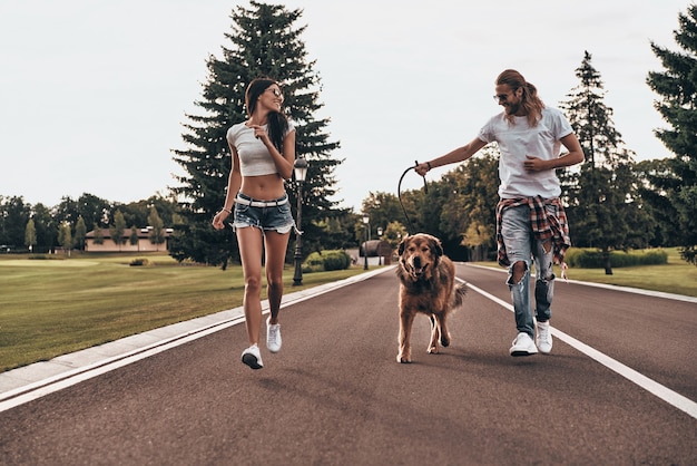 In een richting. Volledige lengte van een mooi jong stel dat met hun hond rent terwijl ze tijd buitenshuis doorbrengen