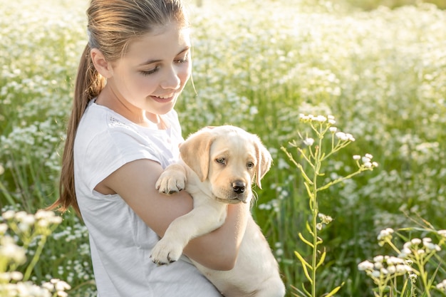 In een veld met bloemen houdt het meisje haar armen vast en kijkt liefdevol naar haar Labrador-puppy