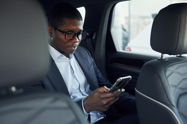 In glazen Jonge Afro-Amerikaanse zakenman in zwart pak zit in de auto