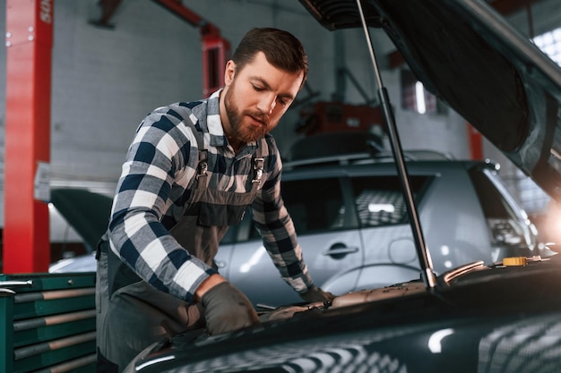 Foto in handschoenen auto repareren man in uniform werkt in de autosalon