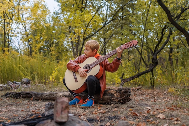 In het herfstpark zit de padvinder op een boomstam met een gitaar in zijn handen