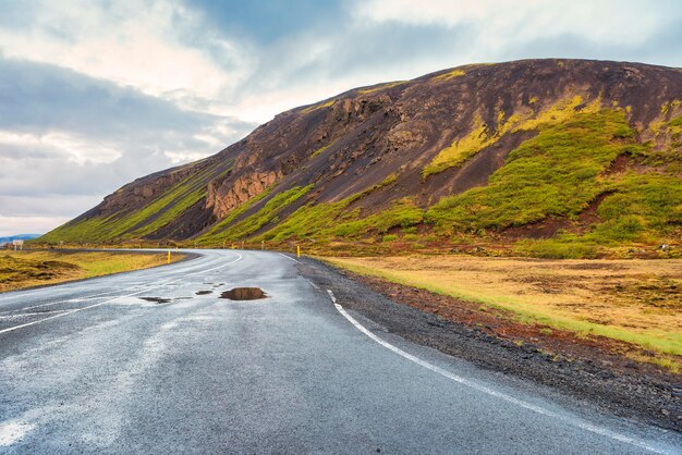 In het midden van een wijd open lege weg, omringd door bergen in IJsland