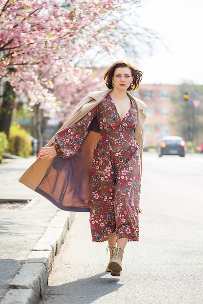 In het voorjaar loopt een vrouw langs een bloeiende straat met sakurabomen. Een meisje in een lange, elegante vintage jurk van zijde loopt tussen de bloeiende bomen