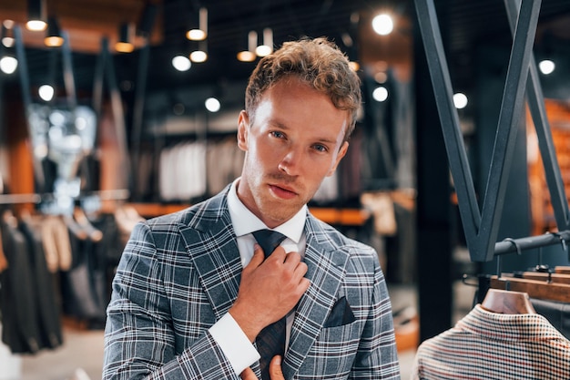 In jasje met stropdas Jonge kerel in moderne winkel met nieuwe kleren Elegante dure kleding voor mannen