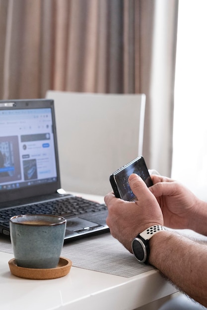 in mannelijke handen een smartphone op de achtergrond van een laptop aan een tafel in de kamer