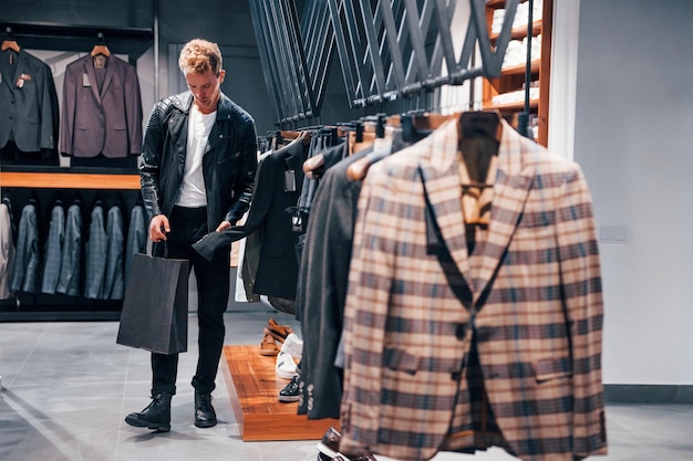 In mooie zwarte jas Jonge kerel in moderne winkel met nieuwe kleren Elegante dure kleding voor mannen