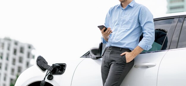 In pak geklede vooruitstrevende zakenman bekijkt de batterijstatus van EV-auto's vanaf zijn telefoon
