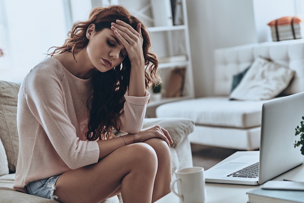 In slechte staat. Zieke jonge vrouwen die hoofdpijn hebben terwijl ze thuis op de bank zitten