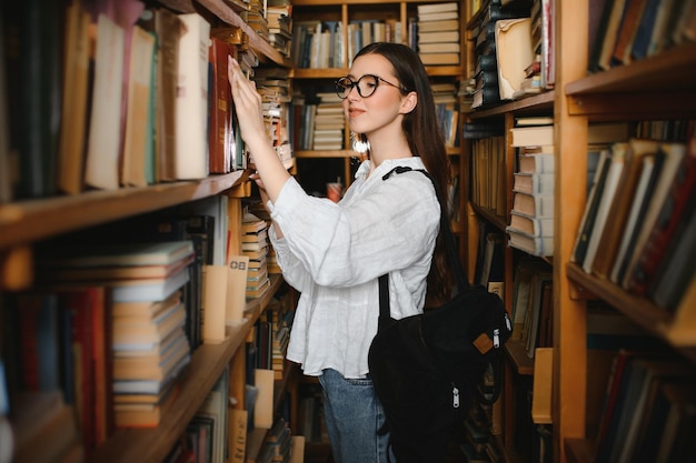 Фото В библиотеке симпатичная ученица с книгами работает в библиотеке средней школы